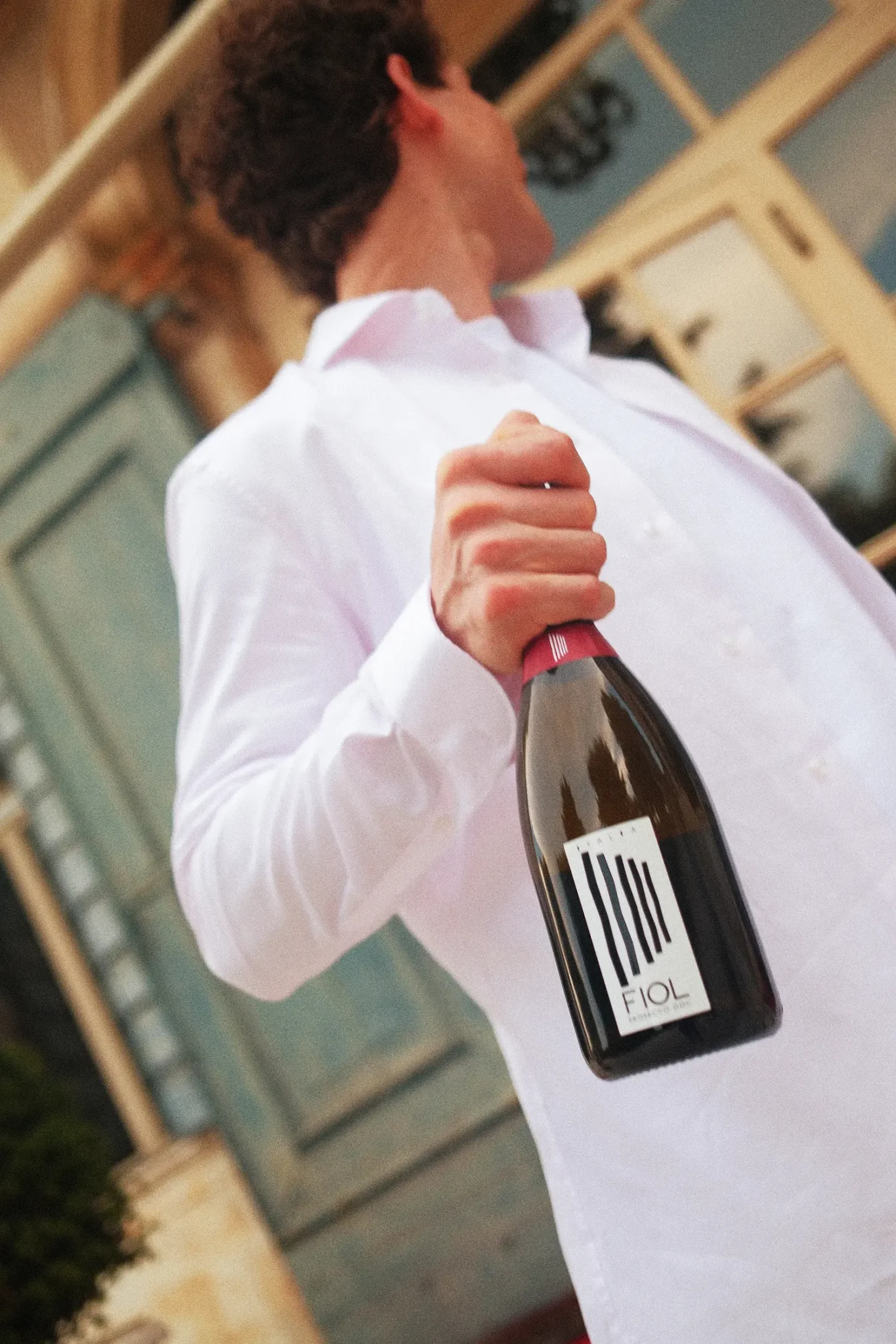Uomo in camicia bianca ripreso dal basso mentre tiene in mano una bottiglia di FIOL Prosecco.